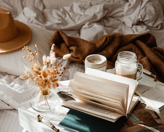 Cozy bedroom scene with a book, plants, and beverages.
